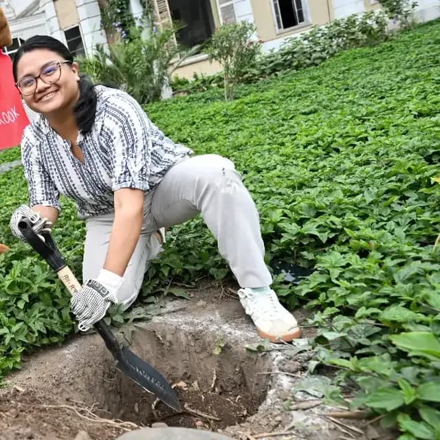 Una ARMY con guantes cava con una pala el hoyo de un árbol, rodeada de vegetación.